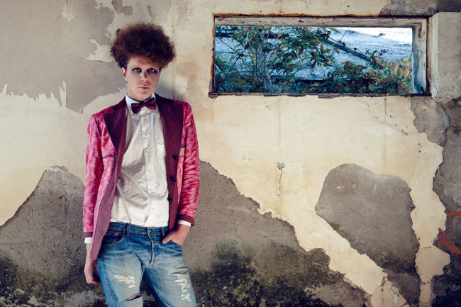 curly boy wearing a pink jacket white shirt and jeans